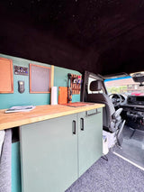 Unique RV rental interior featuring a custom camper van kitchen with teal walls, wood counter, and a stunning starry ceiling.