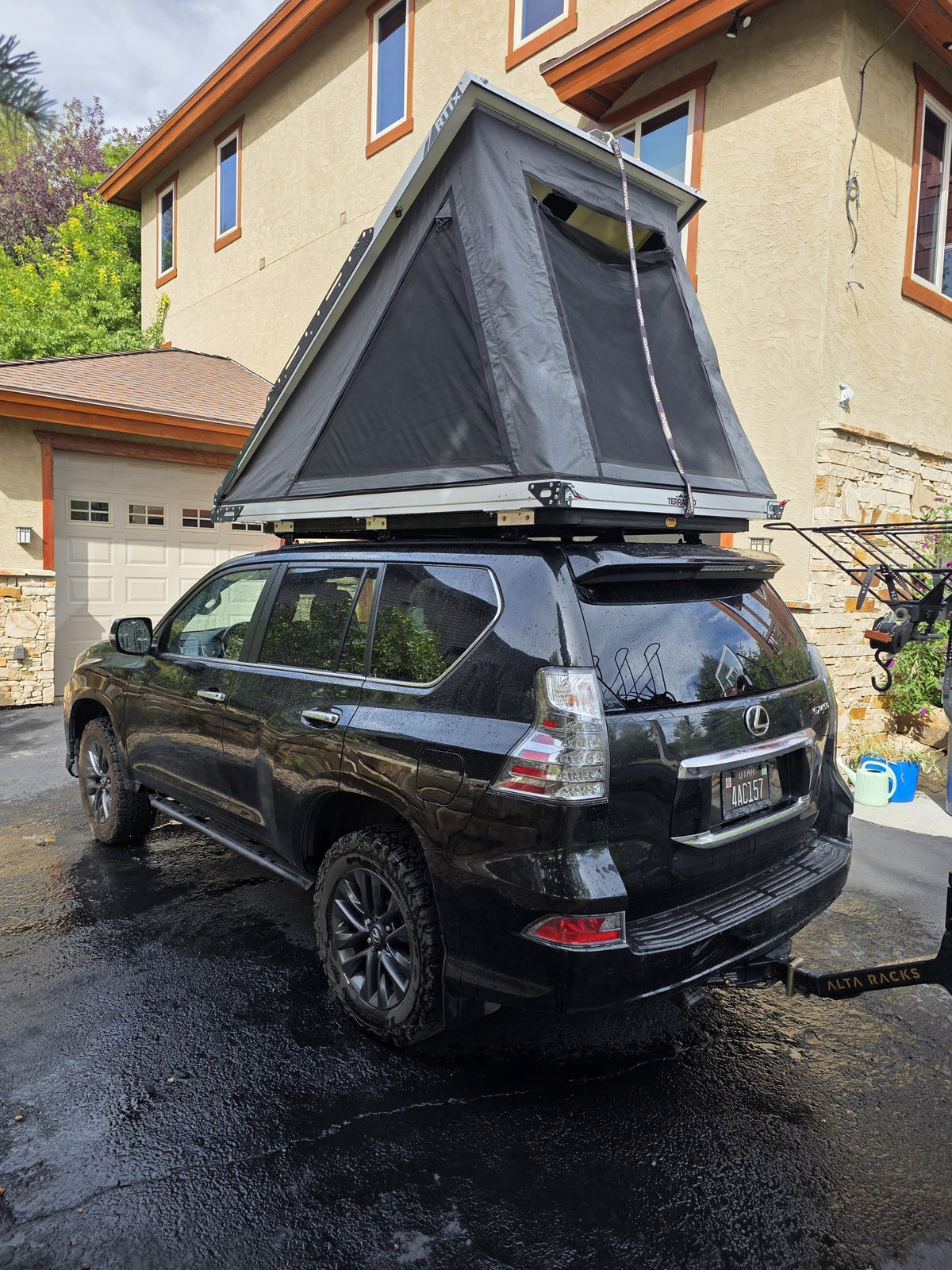 Rear three-quarter view of the Terrapod RTTx XL deployed on the vehicle in a driveway, showing the tent body extended, the rainfly overhead and the aluminium shell tray beneath — photo 11