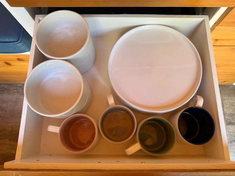 Essential RV rental kitchenware: white bowls, a plate, and various mugs neatly stored in a drawer. — photo 16