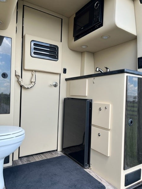 RV rental interior featuring a beige kitchen with microwave, sink, mini-fridge, and a separate bathroom door with toilet visible.