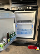 Inside an RV rental: an open refrigerator with beverages, alongside kitchen controls. Ready for your mobile travels.