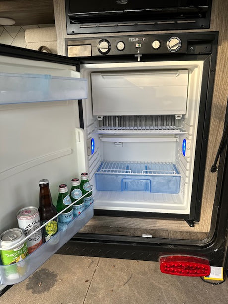 Inside an RV rental: an open refrigerator with beverages, alongside kitchen controls. Ready for your mobile travels.
