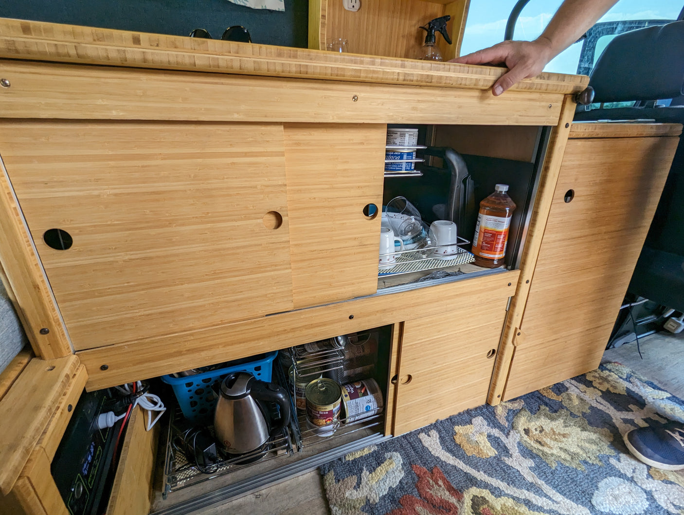 RV rental kitchen: sleek bamboo cabinets, sliding doors reveal dishes, kettle & power station for compact living.