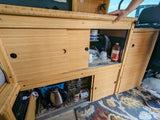 RV rental kitchen: sleek bamboo cabinets, sliding doors reveal dishes, kettle & power station for compact living.