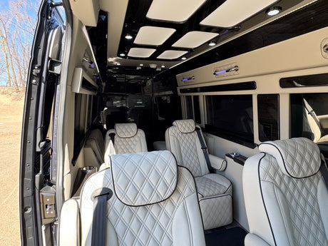Inside a luxurious RV rental: spacious interior with white quilted leather seats, ambient lighting, and sleek black finishes.