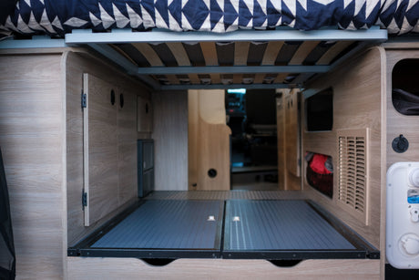 Inside an **rv rental**: organized under-bed **storage** in a **campervan**. Features wooden interior, bed frame, and utility connections.