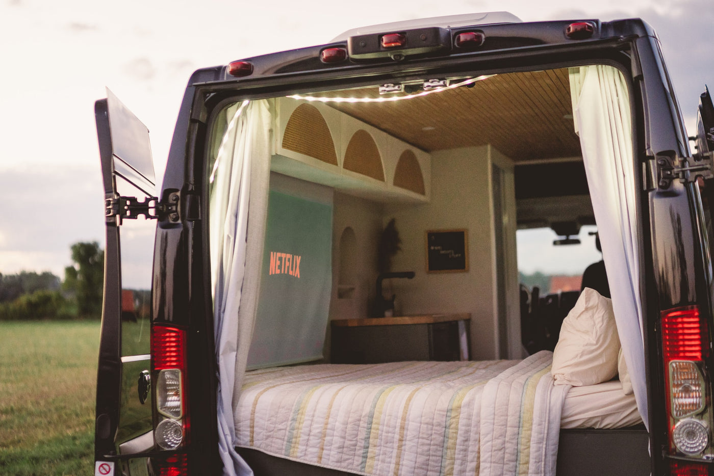 Enjoy cozy comfort in this rv rental. Rear view shows a bed, Netflix projection, and kitchen. Perfect for van life adventures. — photo 11