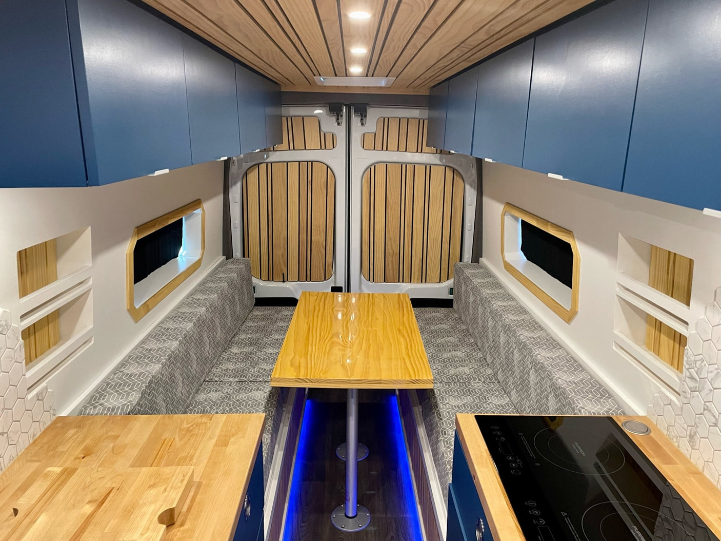 Bright RV rental interior with a dining table, kitchen, overhead cabinets, and comfy benches.