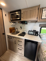 Compact RV rental kitchen features microwave, sink, cooktop, fridge, toaster oven, & coffee maker. Modern design for trips.