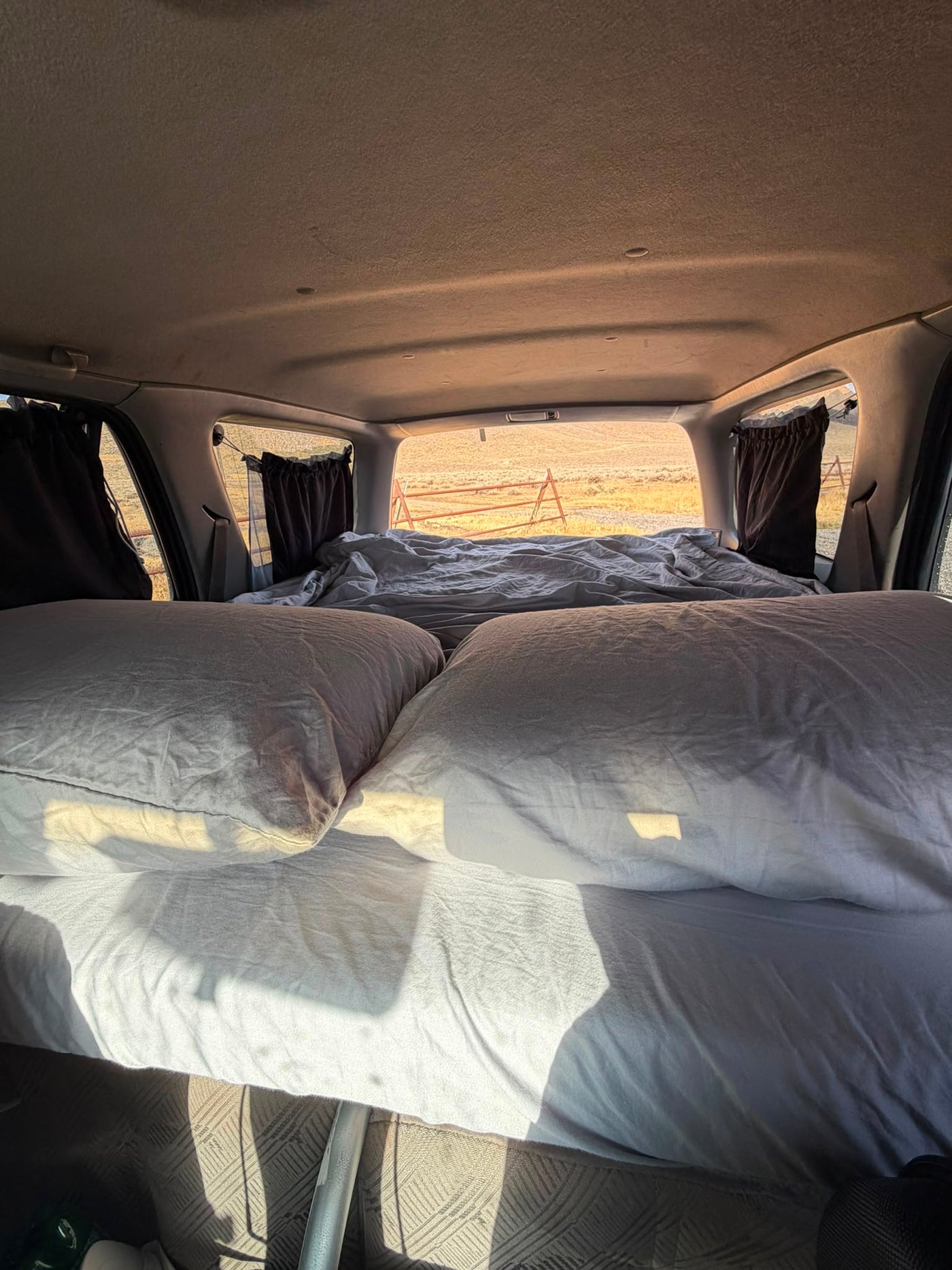 Interior sleeping platform made up for two, blackout window curtains, rear hatch window looking out over open country at sunrise — photo 6