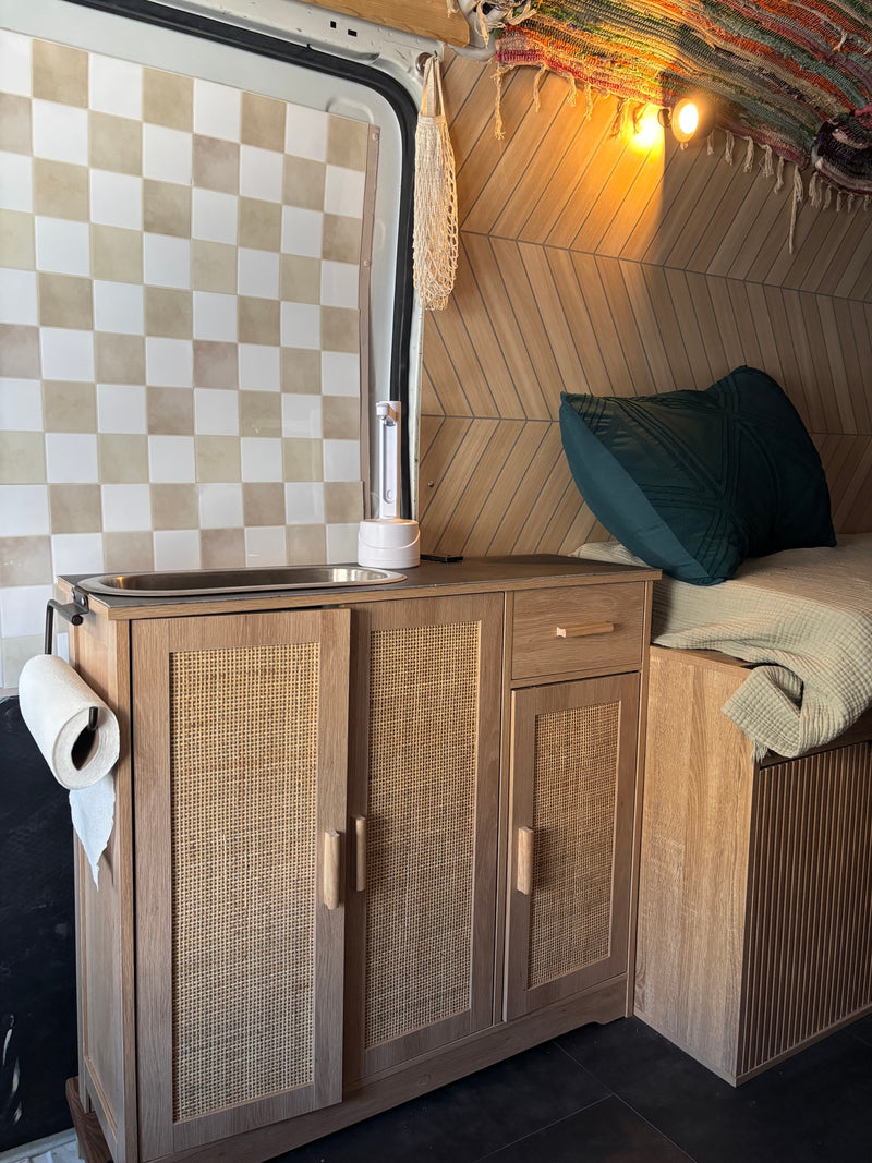 Inside a stylish rv rental: kitchenette with sink, woven cane cabinets, and a cozy bed with a green pillow. — photo 3
