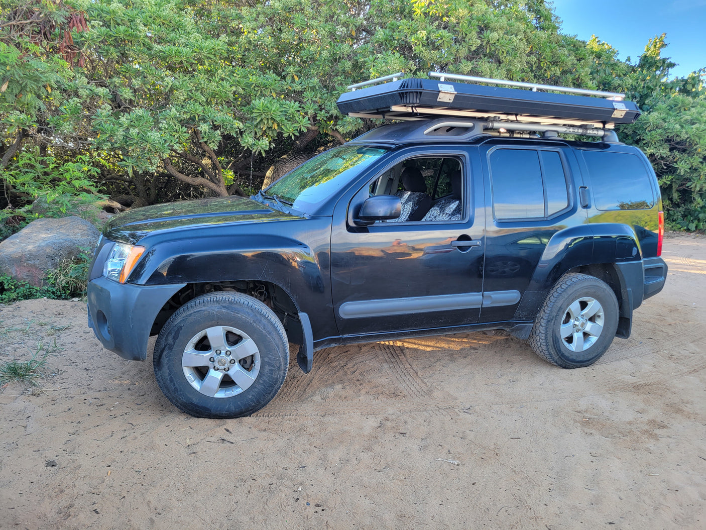 Black SUV with rooftop tent on a dirt road, surrounded by trees. Great for an rv rental outdoor adventure.