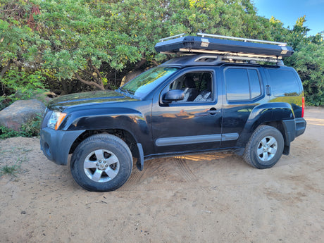Black SUV with rooftop tent on a dirt road, surrounded by trees. Great for an rv rental outdoor adventure.