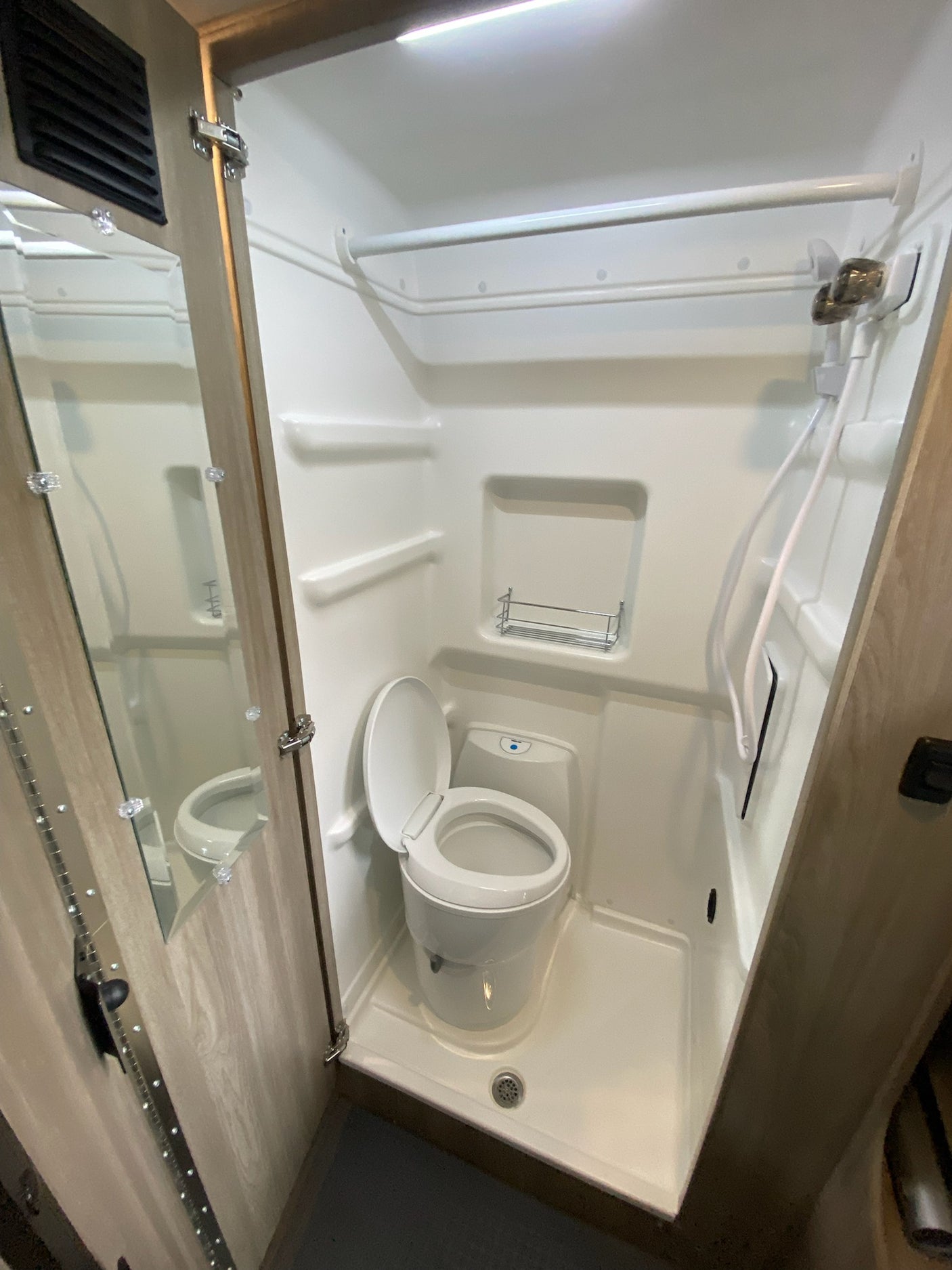Compact RV rental wet bath, featuring a toilet, shower, and mirrored cabinet, ideal for travel.