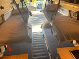 Inside a comfy RV rental: two neatly made beds, wood cabinets, and a partial kitchen area, looking out the rear.