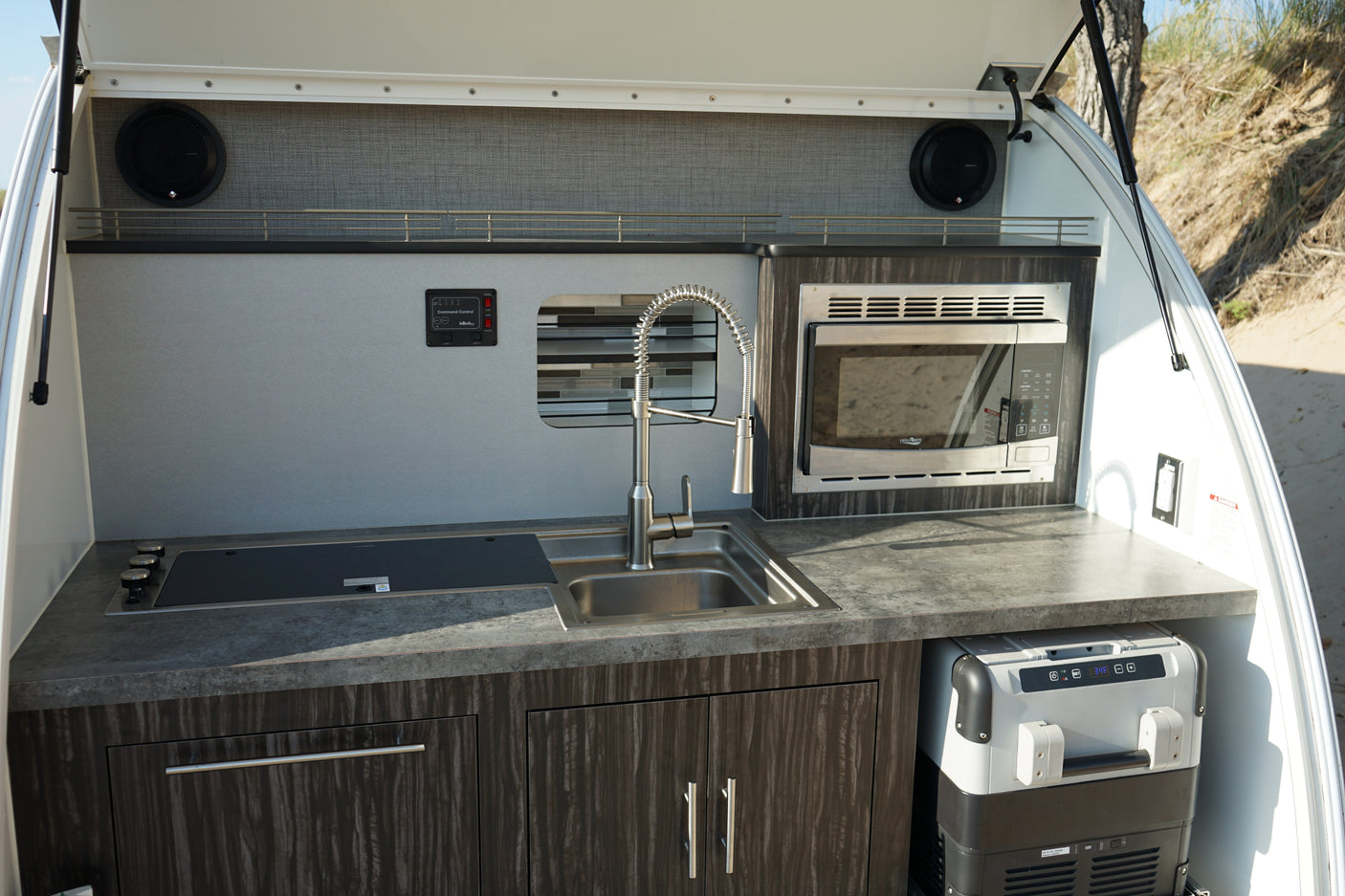 RV rental outdoor kitchen with sink, cooktop, microwave, speakers, and portable fridge, designed for convenience.
