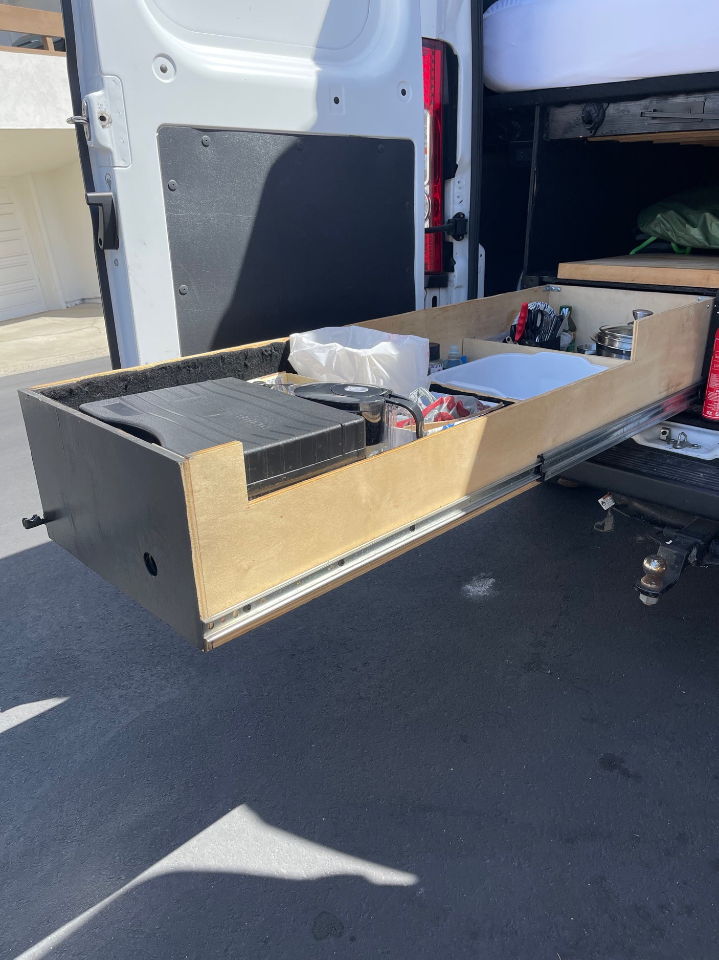 This rv rental features an extended rear pull-out kitchen drawer, organized with a portable stove, water filter, and cooking essentials for camper van trips.