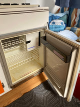 This Dometic RV refrigerator, with its door open, shows a compact interior, freezer, and shelves, ready for your rv rental.