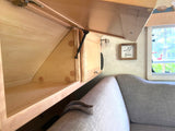 Inside an RV rental: view of open wooden overhead storage, a small cabinet, and a gray sofa with a "wild and free" sign.