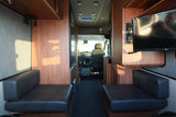 Interior of an rv rental: opposing dark benches, wood cabinetry, a TV, and the driver's cabin in view.