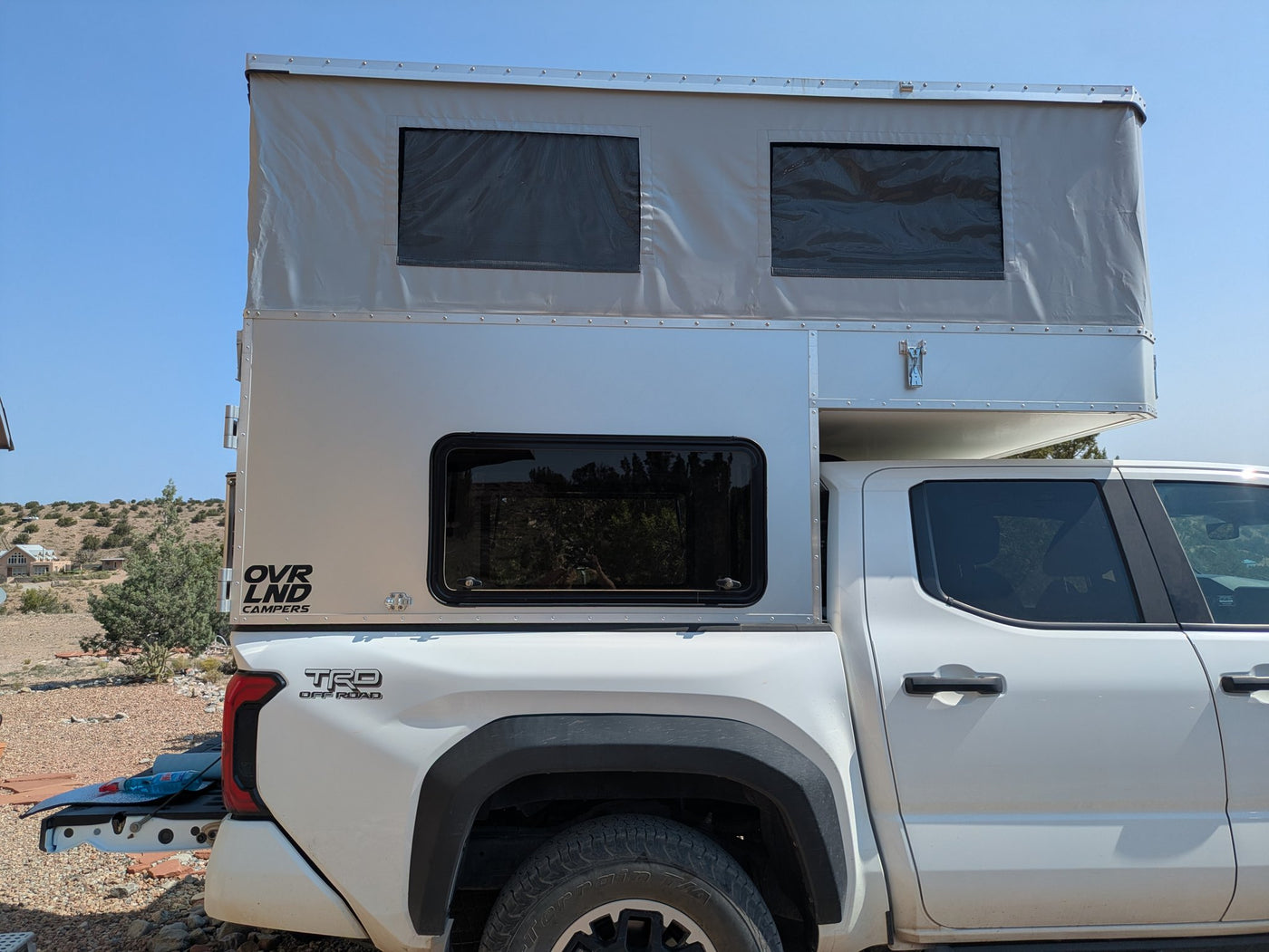 OVRLND Bread N Butter pop-top camper with the roof raised on a white Toyota Tacoma, passenger-side rear three-quarter view — photo 2