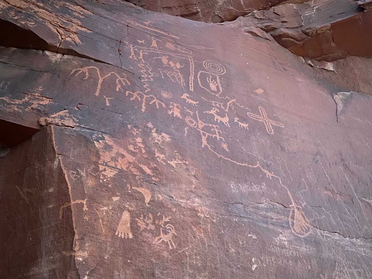Ancient petroglyphs on dark rock, featuring human and animal figures. Discover this outdoor art on your next RV rental adventure.