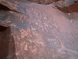 Ancient petroglyphs on dark rock, featuring human and animal figures. Discover this outdoor art on your next RV rental adventure.