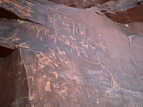 Ancient petroglyphs on dark rock, featuring human and animal figures. Discover this outdoor art on your next RV rental adventure.