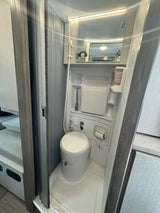 Compact RV rental wet bath, featuring toilet, shower, sink, and mirror for travel convenience