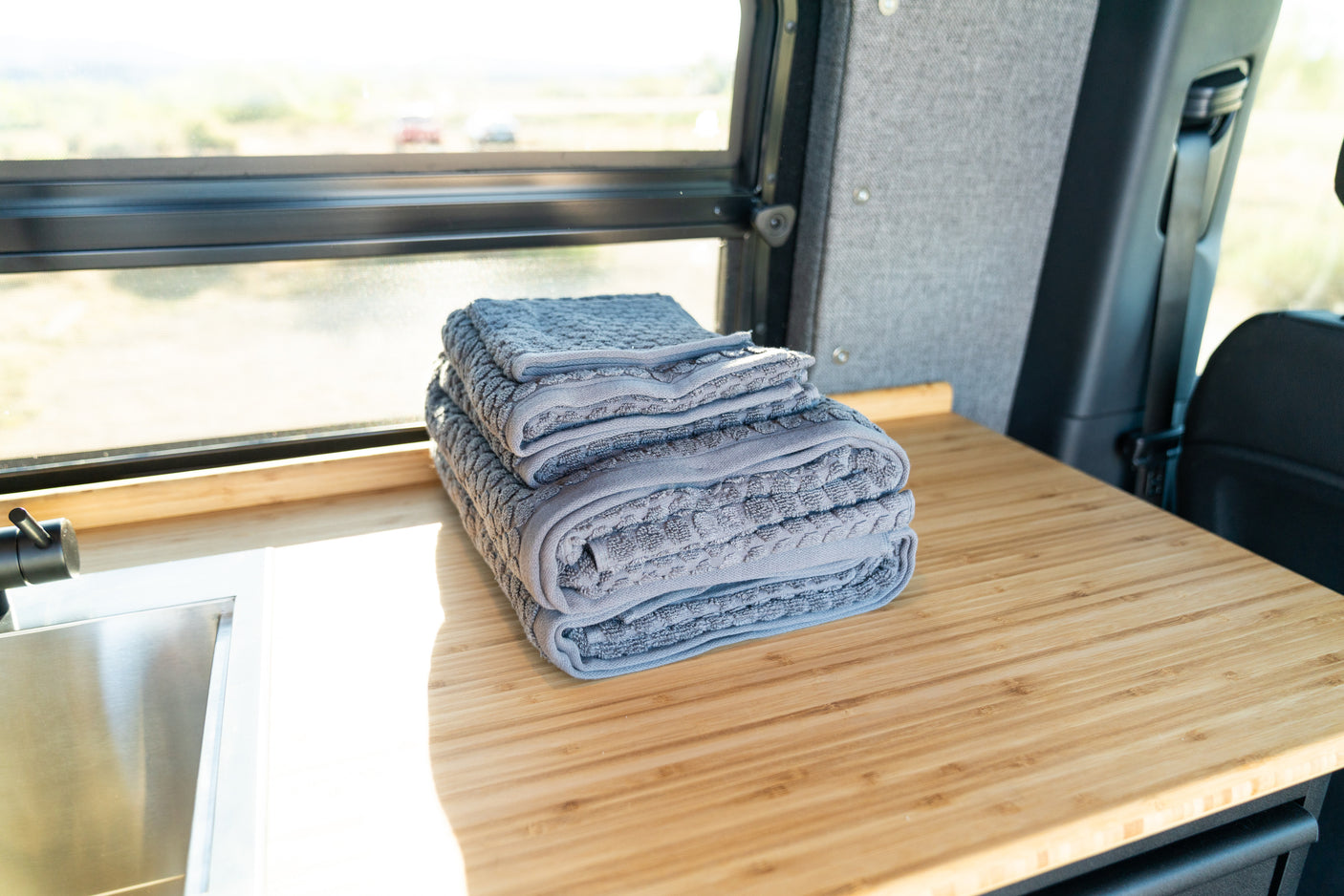 Stack of gray towels on a wooden counter with a sink and window, inside an RV rental.