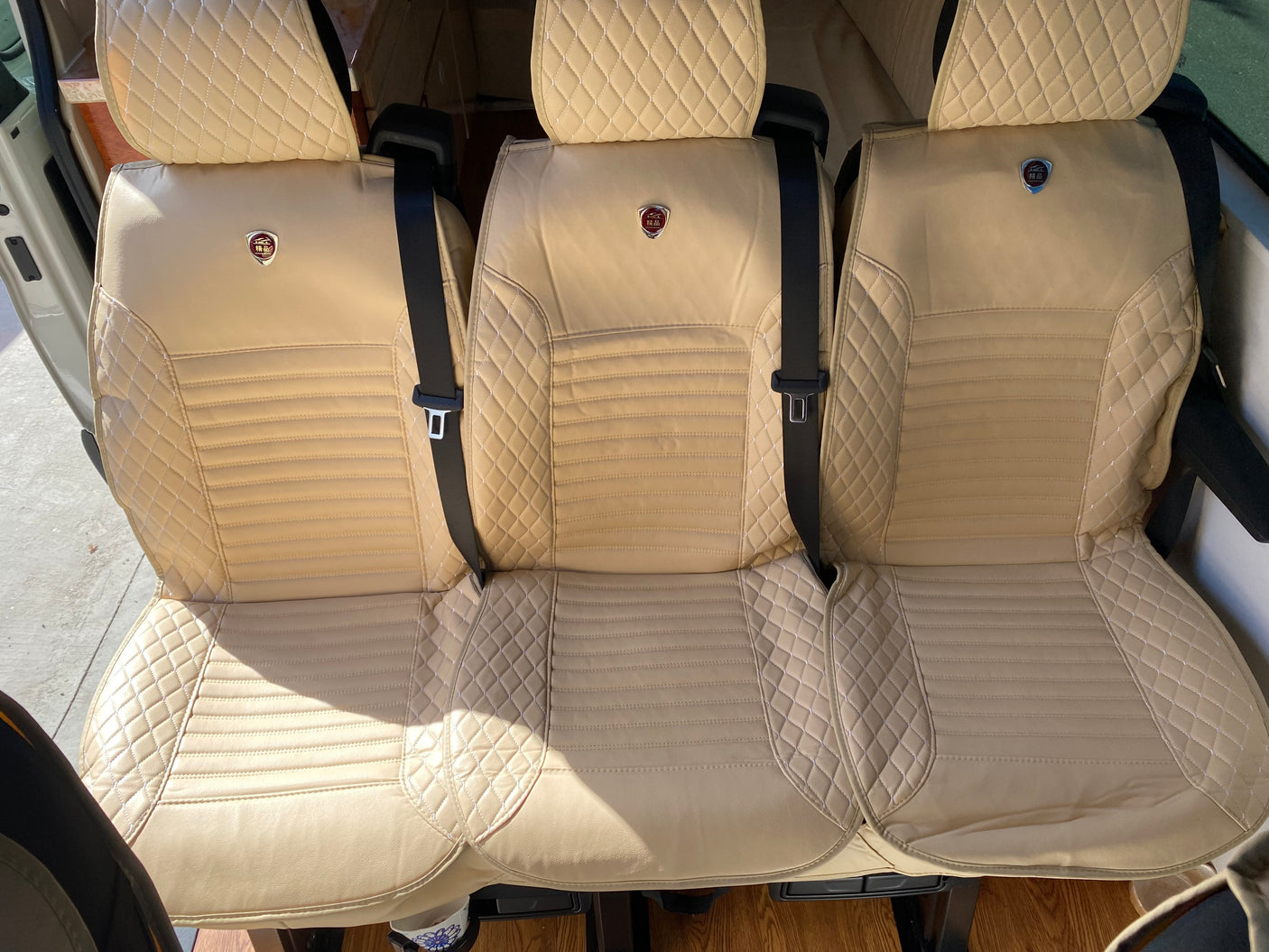 Inside an RV rental: three luxurious, diamond-stitched beige seats with seatbelts for comfortable travel.