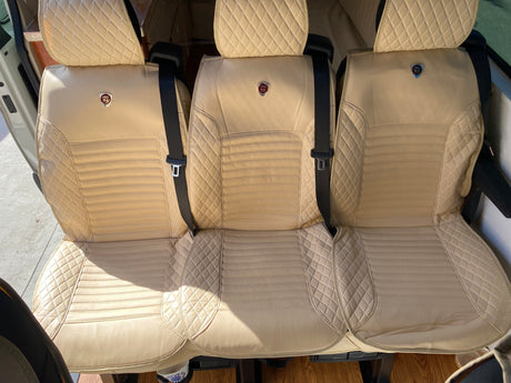 Inside an RV rental: three luxurious, diamond-stitched beige seats with seatbelts for comfortable travel.