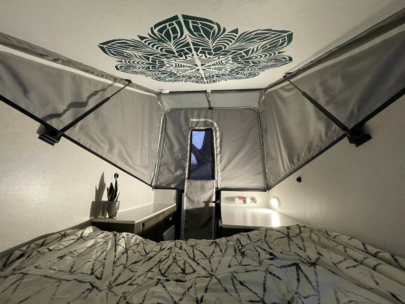 Inside a cozy RV rental: a patterned bed, mandala ceiling art, and gray pop-up fabric walls.