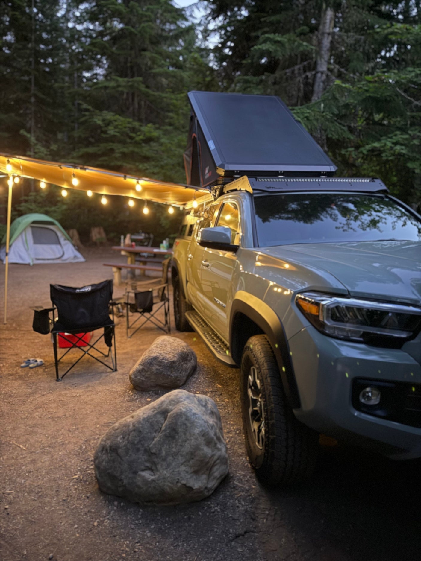 Cozy night camping setup: a truck with a rooftop tent & awning, lit by string lights, perfect for your rv rental trip.