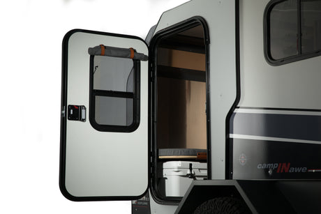 Compact RV rental: Open door shows interior bed, cooler, and roll-up shade; side has sleek stripes.