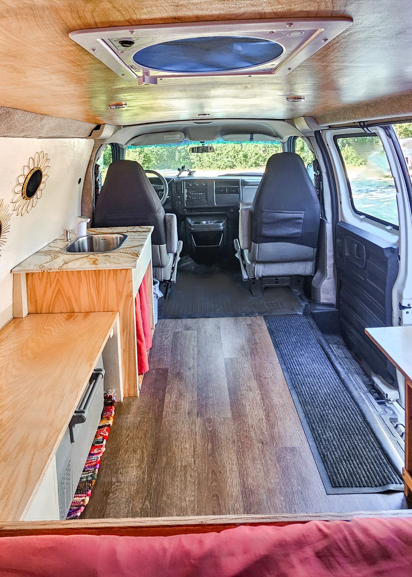 Inside a functional RV rental: view from the bed towards the custom kitchen, wood flooring, and front cockpit. Ideal for travel.
