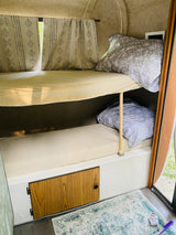 Bunk beds inside an RV rental, offering a cozy sleep space with floral pillows & patterned curtains.