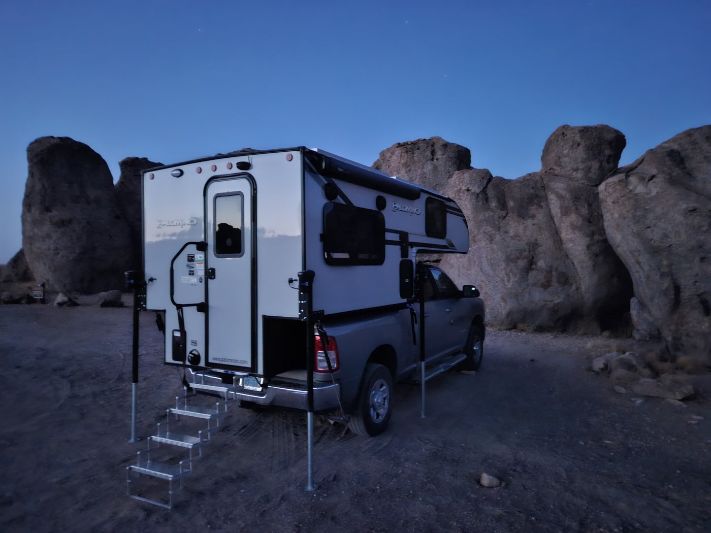 A truck camper, perfect for an RV rental, parked among large rocks under a twilight sky, ready for outdoor adventure. — photo 14
