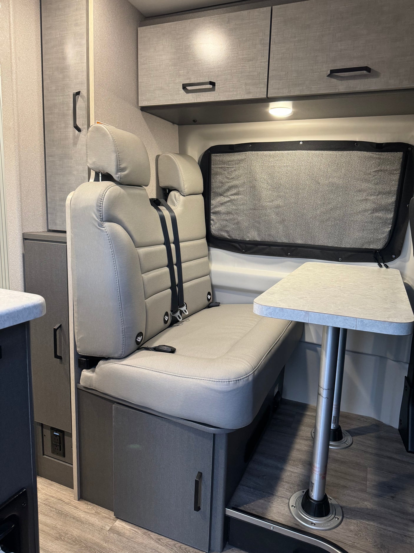 Inside this RV rental: a grey dinette with two belted seats, removable table, and overhead cabinets for comfy journeys.