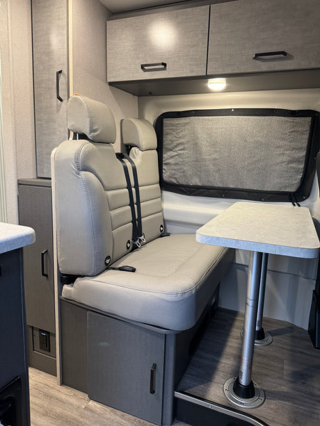 Inside this RV rental: a grey dinette with two belted seats, removable table, and overhead cabinets for comfy journeys.