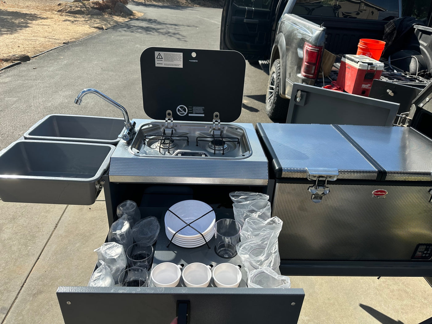 Enjoy an rv rental adventure with this compact camping kitchen featuring a sink, stove, fridge, and organized dish storage. — photo 13
