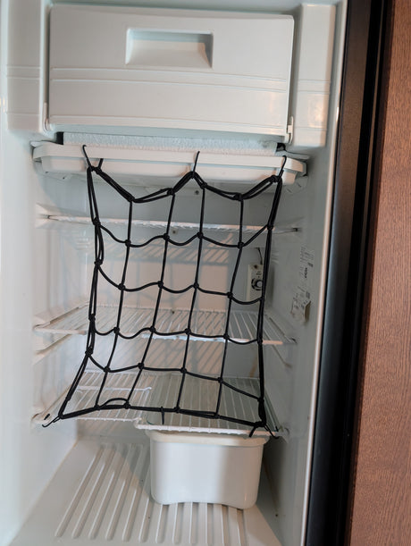 Inside an RV rental fridge: a black cargo net secures items on shelves, preventing movement & spills during travel. Frost on freezer.