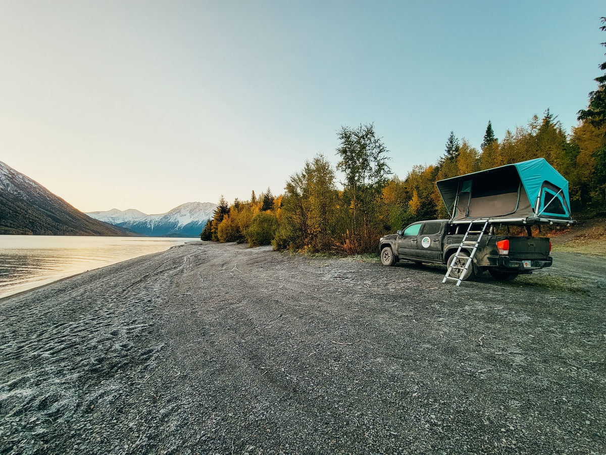 Explore scenic landscapes! This RV rental setup, a truck with a rooftop tent, offers lakeside camping near snowy mountains. — photo 3