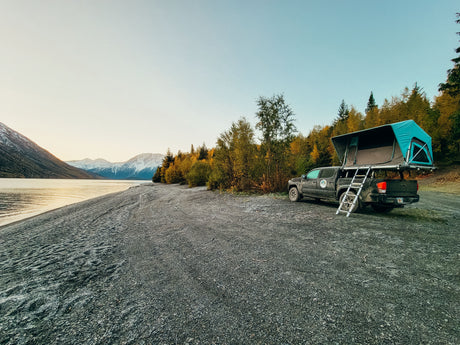 Explore scenic landscapes! This RV rental setup, a truck with a rooftop tent, offers lakeside camping near snowy mountains.