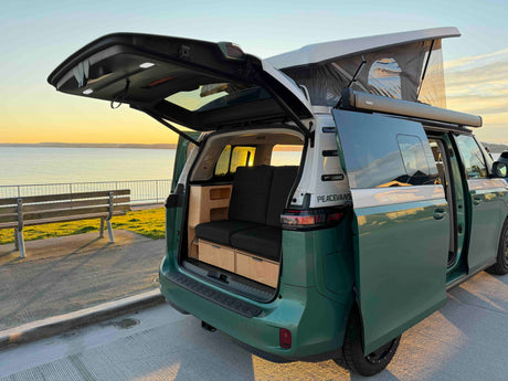 Scenic sunset view behind a green pop-top camper van, showing its open trunk, cozy custom interior, and awning. Great rv rental option.