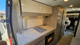 This rv rental features a well-equipped compact kitchen with a sink, microwave, overhead storage, and comfortable living space.