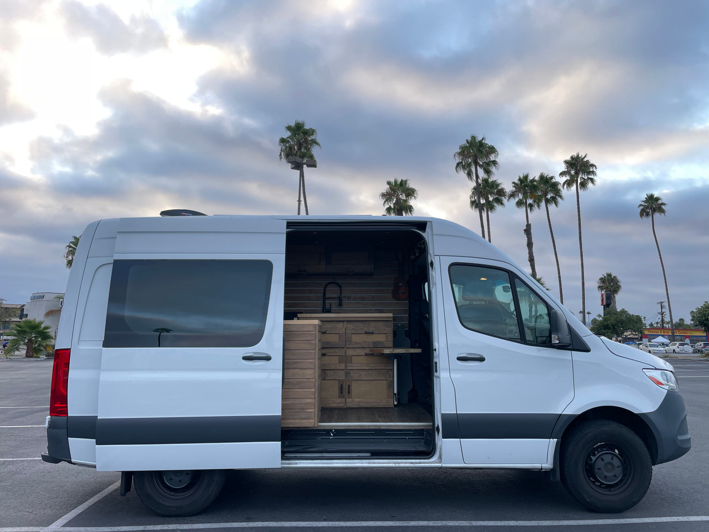 This custom white camper van, ideal for rv rental trips, reveals its detailed wood interior parked under palm trees.