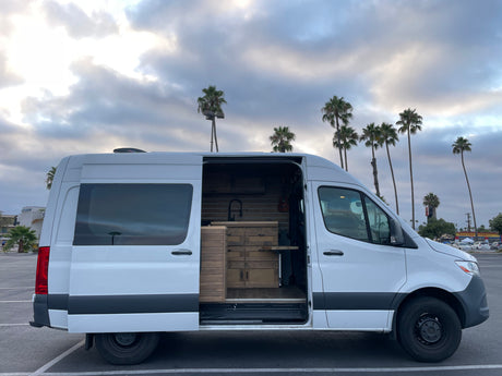 This custom white camper van, ideal for rv rental trips, reveals its detailed wood interior parked under palm trees.