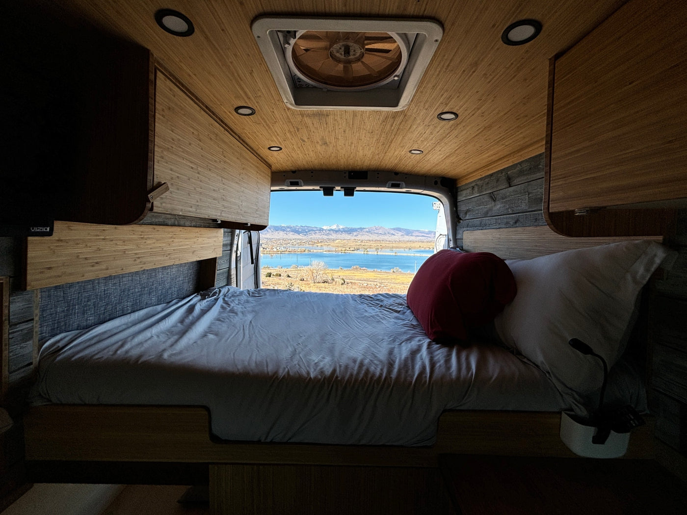 RV rental interior: A cozy bed faces a stunning view of a lake, bridge, and snowy mountains. — photo 15