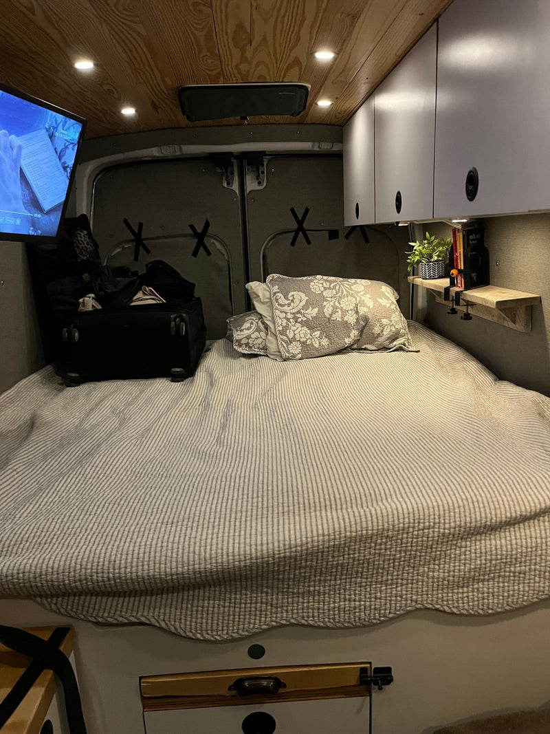 Cozy RV rental interior shows a comfortable bed, TV, overhead cabinets, and wooden ceiling in a camper van. — photo 6